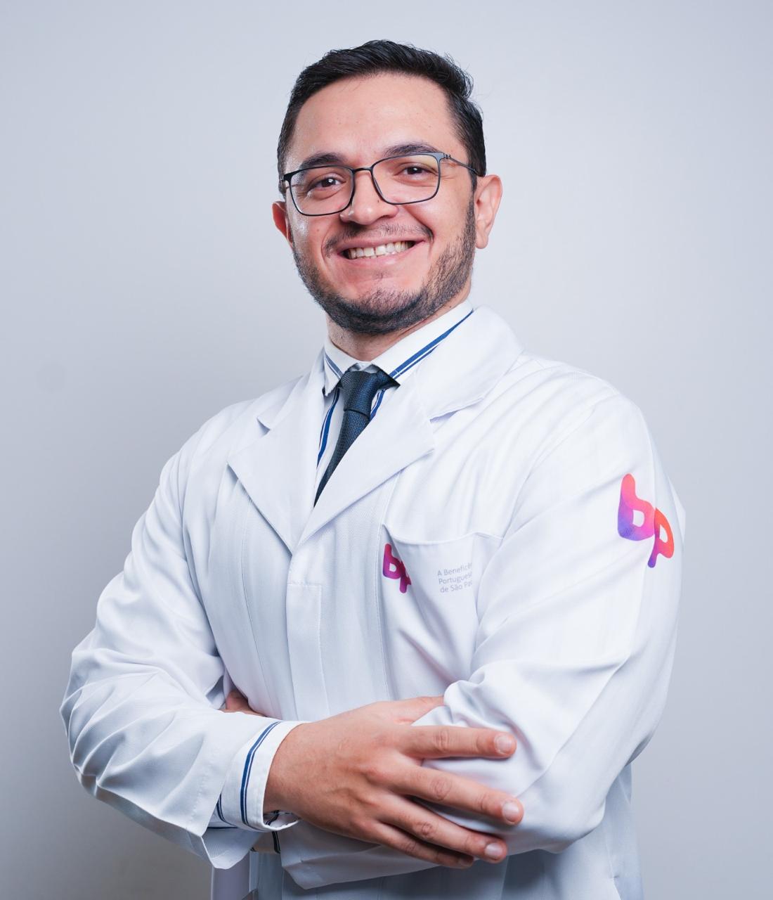 Dr. Maximiliano Guedes, médico oncologista, sorrindo e usando jaleco branco